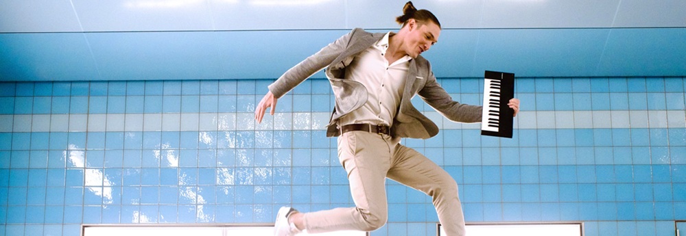 Andreas Langsch. Klavierkabarettist. Künstler in einem U-Bahnhof fotografiert, springt dynamisch hoch und hält ein ein kleines Keyboard unterm Arm.